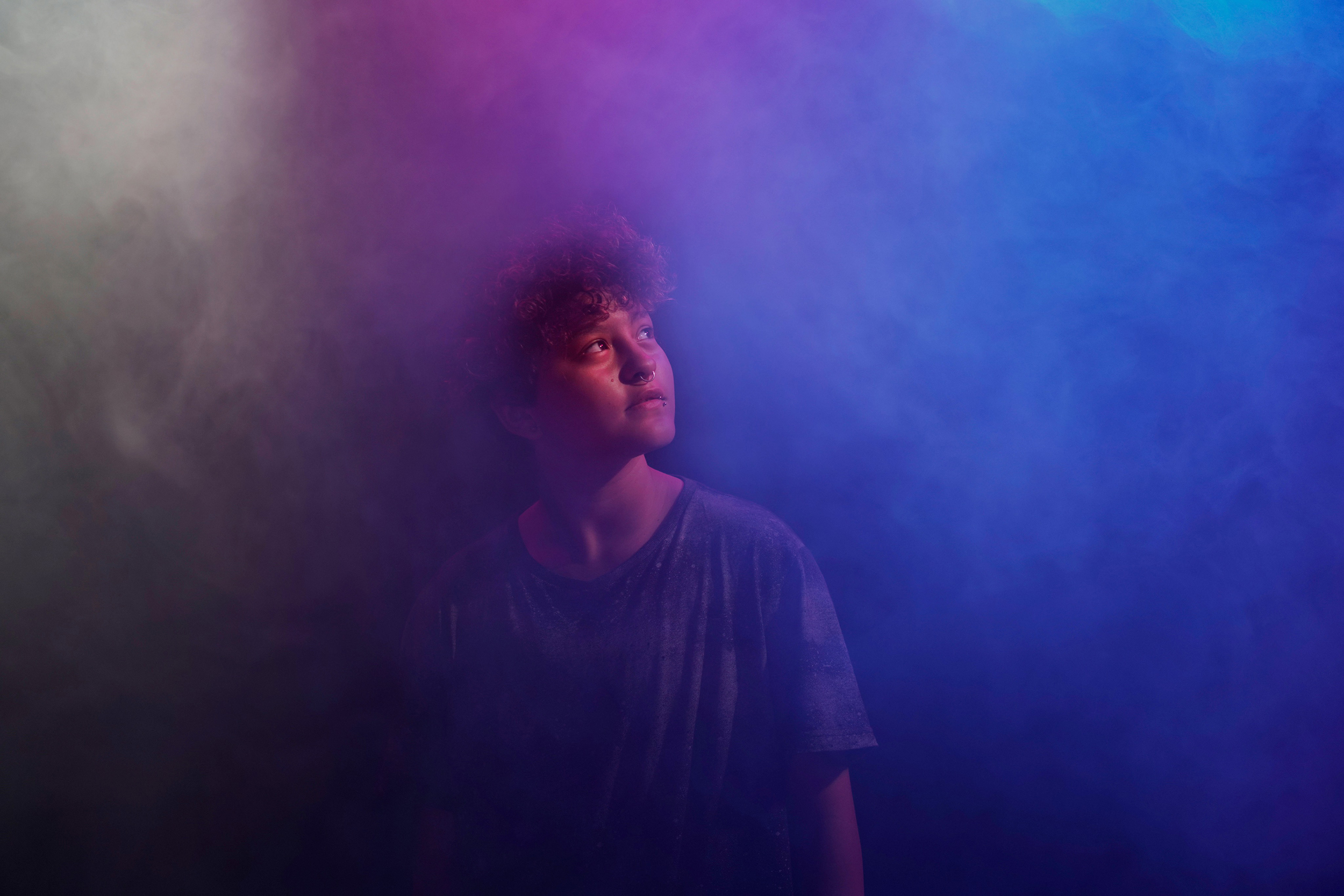 Ethan steht umhüllt von lila-blauem Nebel in einem dunklen Raum und blickt nach rechts oben.